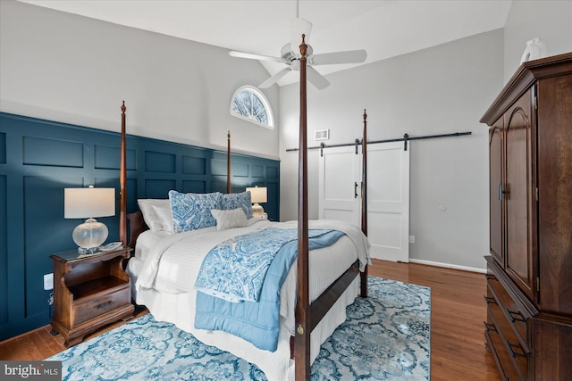 bedroom with a barn door, wood finished floors, visible vents, and a decorative wall