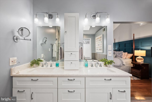 bathroom with double vanity, ensuite bath, a sink, and wood finished floors