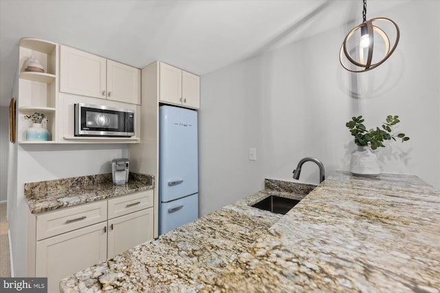 kitchen featuring light stone counters, freestanding refrigerator, stainless steel microwave, and a sink