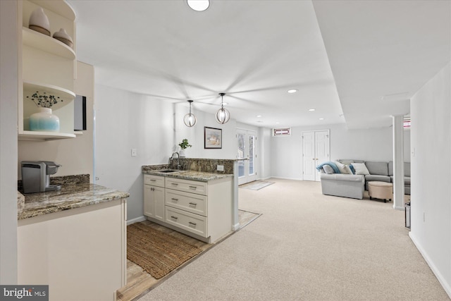 kitchen featuring light carpet, light stone counters, open floor plan, a peninsula, and a sink