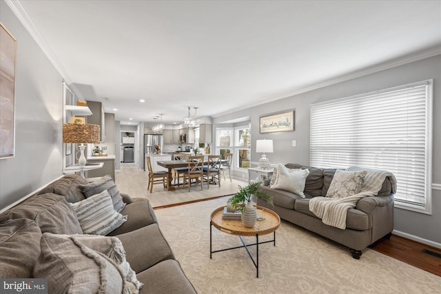 living area with light wood-style floors, a notable chandelier, ornamental molding, and baseboards