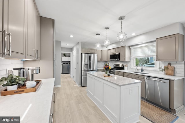 kitchen featuring gray cabinetry, stainless steel appliances, a sink, a center island, and decorative backsplash