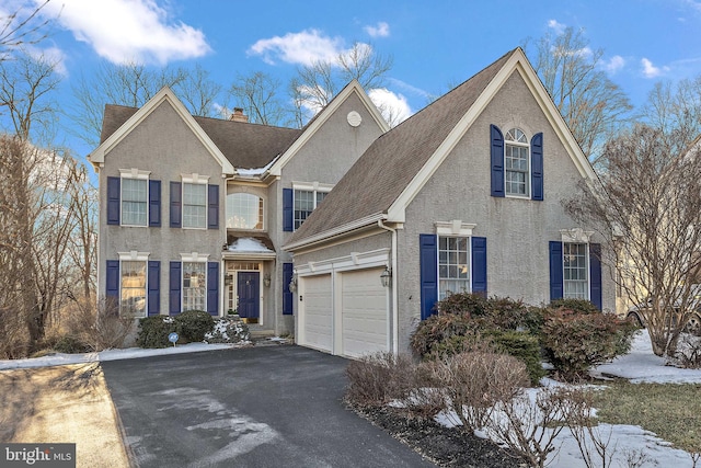 view of front facade with aphalt driveway, a chimney, an attached garage, and stucco siding