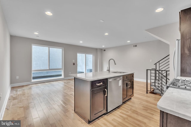 kitchen with an island with sink, sink, stainless steel dishwasher, light stone countertops, and light hardwood / wood-style flooring