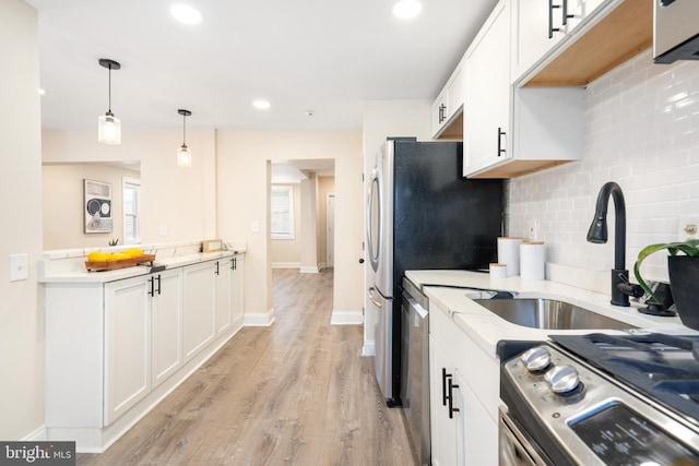 kitchen featuring stainless steel appliances, a sink, decorative light fixtures, and white cabinets