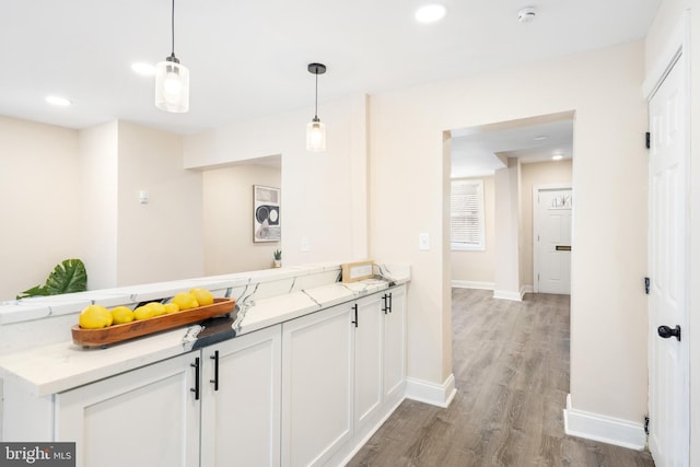 kitchen with light stone counters, white cabinets, hanging light fixtures, and wood finished floors