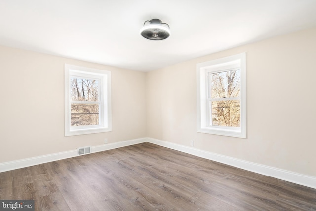 unfurnished room featuring dark wood-style floors, visible vents, and baseboards