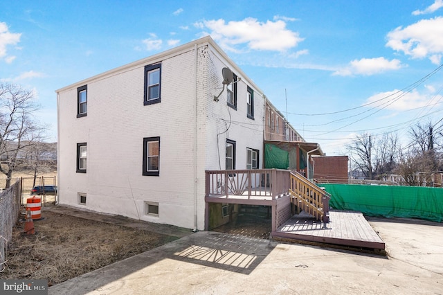 rear view of house featuring brick siding, fence, and a wooden deck