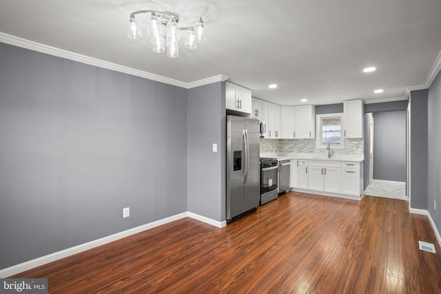 kitchen with sink, white cabinets, ornamental molding, stainless steel appliances, and dark wood-type flooring