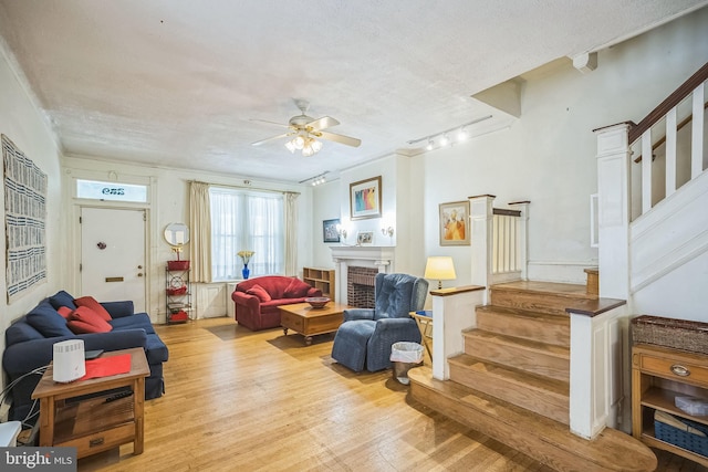 living area with light wood-style flooring, stairs, a fireplace, and a textured ceiling