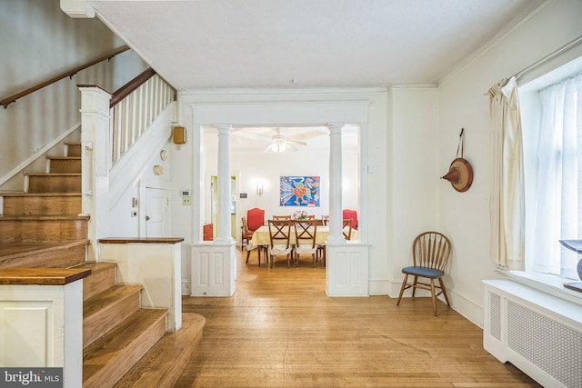 interior space with radiator, ornate columns, light wood-type flooring, and stairway