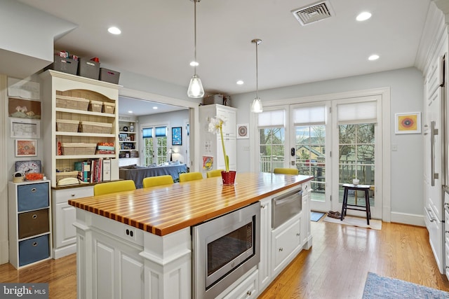 kitchen with butcher block counters, decorative light fixtures, stainless steel microwave, a kitchen island, and white cabinets