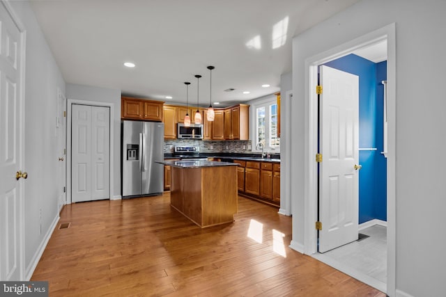 kitchen with pendant lighting, light hardwood / wood-style flooring, stainless steel appliances, a center island, and decorative backsplash