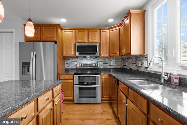 kitchen featuring pendant lighting, sink, dark stone countertops, stainless steel appliances, and light hardwood / wood-style flooring