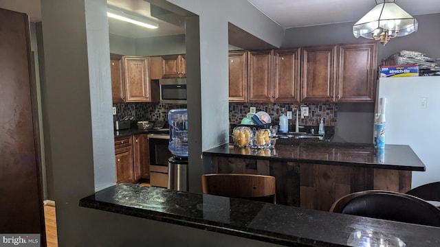 kitchen featuring pendant lighting, dark stone countertops, stainless steel appliances, tasteful backsplash, and kitchen peninsula