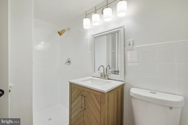 bathroom with tiled shower, vanity, toilet, and tile walls