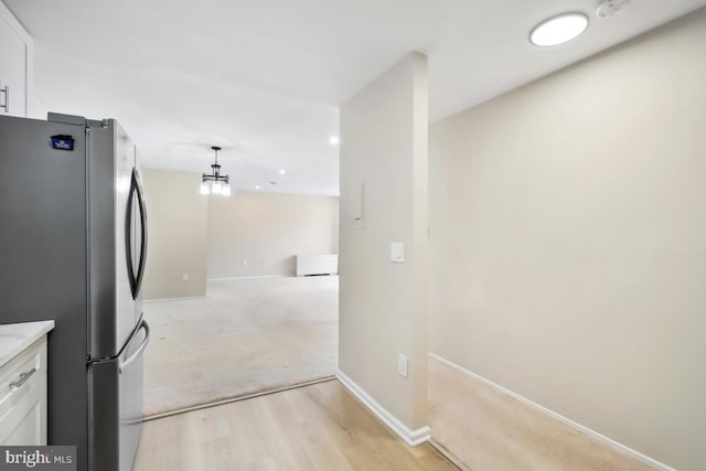 kitchen with stainless steel refrigerator, white cabinetry, light hardwood / wood-style floors, and hanging light fixtures