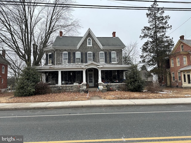 view of front facade with covered porch, a chimney, and stone siding