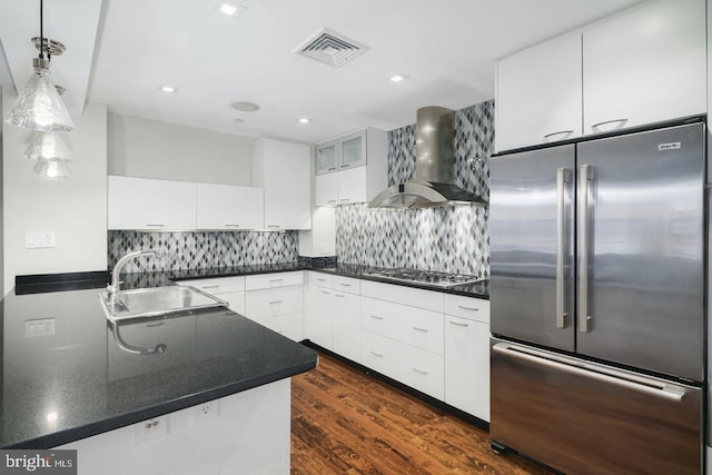 kitchen with pendant lighting, wall chimney range hood, sink, appliances with stainless steel finishes, and white cabinets