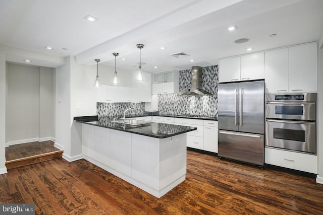 kitchen featuring wall chimney exhaust hood, white cabinetry, stainless steel appliances, and kitchen peninsula