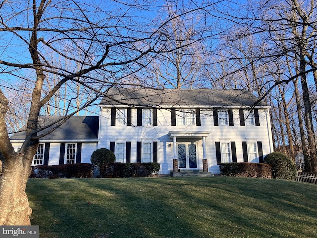 colonial home featuring roof with shingles and a front yard