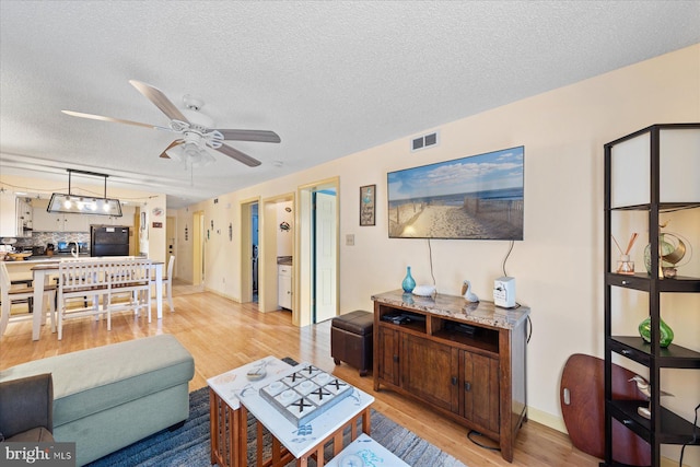 living room featuring ceiling fan, a textured ceiling, and light hardwood / wood-style floors