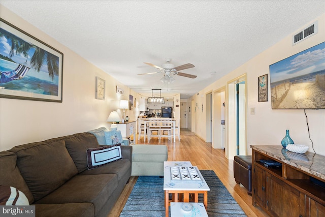 living room with a textured ceiling, light hardwood / wood-style floors, and ceiling fan