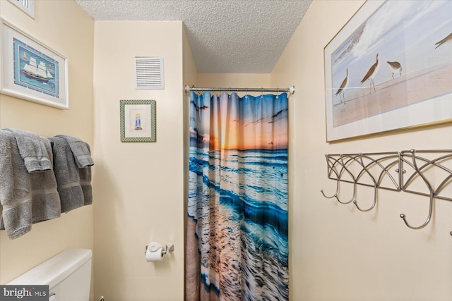 bathroom with a textured ceiling, toilet, and a shower with shower curtain