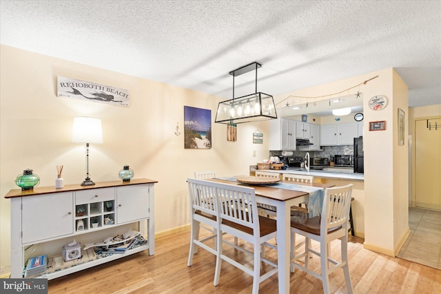 dining space featuring sink, a textured ceiling, and light wood-type flooring