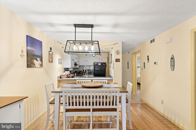 dining room featuring sink, a textured ceiling, and light wood-type flooring