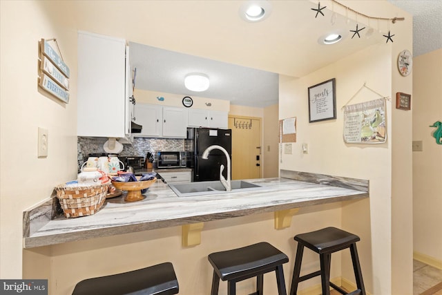 kitchen featuring white cabinetry, a breakfast bar area, backsplash, kitchen peninsula, and black fridge