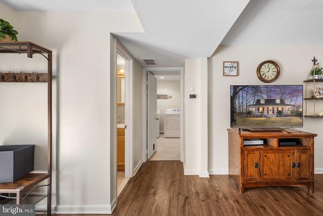 hallway with washer / clothes dryer, wood finished floors, visible vents, and baseboards