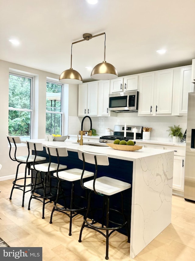 kitchen with an island with sink, white cabinetry, appliances with stainless steel finishes, and pendant lighting