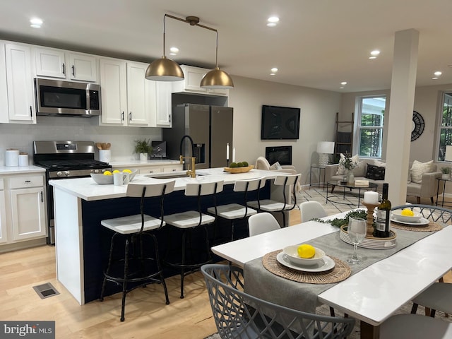 kitchen with stainless steel appliances, open floor plan, hanging light fixtures, light countertops, and an island with sink