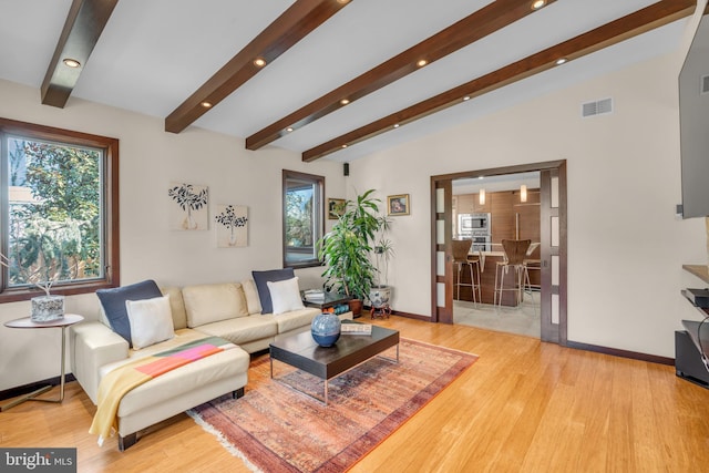 living room featuring light hardwood / wood-style floors, plenty of natural light, and vaulted ceiling with beams