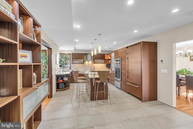 kitchen featuring appliances with stainless steel finishes, tasteful backsplash, hanging light fixtures, a kitchen breakfast bar, and an island with sink