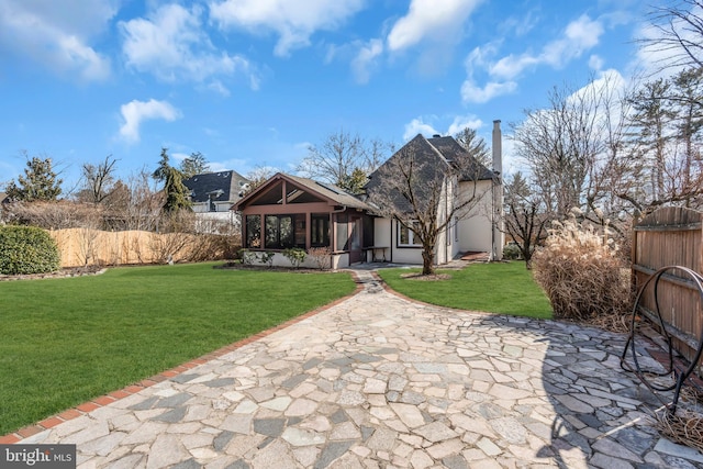 rear view of property with a sunroom, a patio area, and a lawn