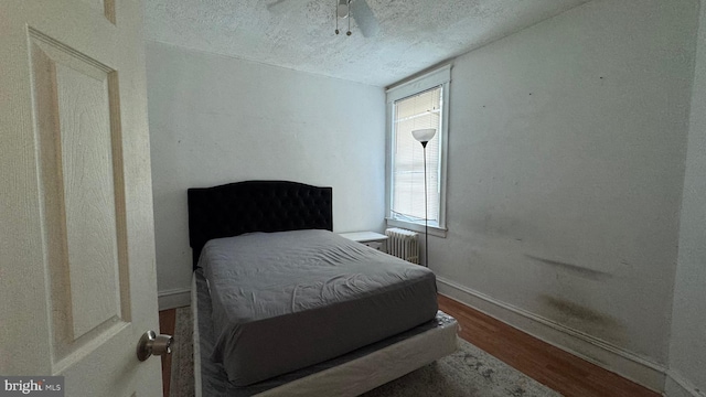 bedroom featuring ceiling fan, radiator, hardwood / wood-style floors, and a textured ceiling