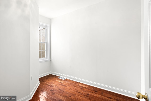 empty room with dark wood-style flooring, visible vents, and baseboards