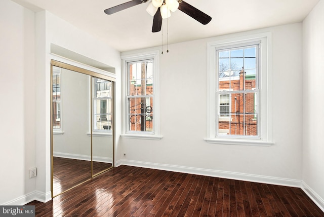 unfurnished bedroom with ceiling fan, a closet, baseboards, and dark wood-style flooring