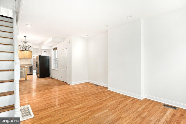 unfurnished living room featuring light wood-style floors, visible vents, stairway, and baseboards