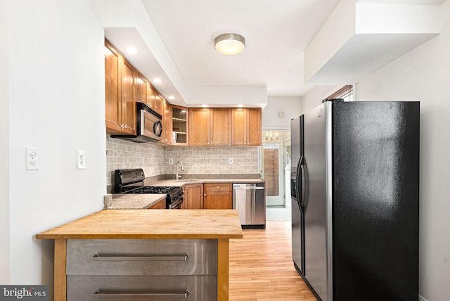 kitchen featuring brown cabinets, glass insert cabinets, a sink, a peninsula, and black appliances