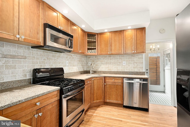 kitchen with glass insert cabinets, appliances with stainless steel finishes, brown cabinets, light stone countertops, and a sink