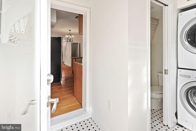 laundry room featuring a chandelier, stacked washer / drying machine, laundry area, and baseboards