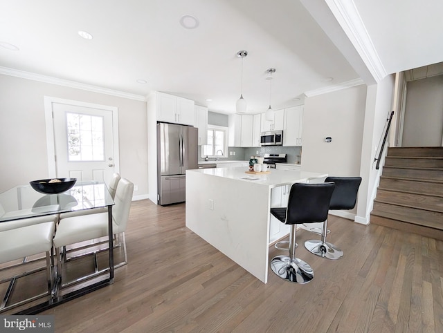 kitchen with white cabinetry, decorative light fixtures, a kitchen island, and appliances with stainless steel finishes