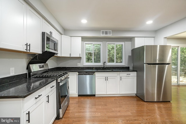 kitchen featuring sink, light hardwood / wood-style flooring, appliances with stainless steel finishes, white cabinetry, and dark stone counters