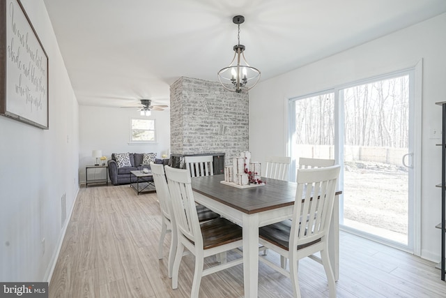 dining space featuring a brick fireplace, ceiling fan with notable chandelier, and light hardwood / wood-style flooring