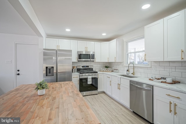 kitchen with appliances with stainless steel finishes, tasteful backsplash, white cabinetry, butcher block counters, and sink