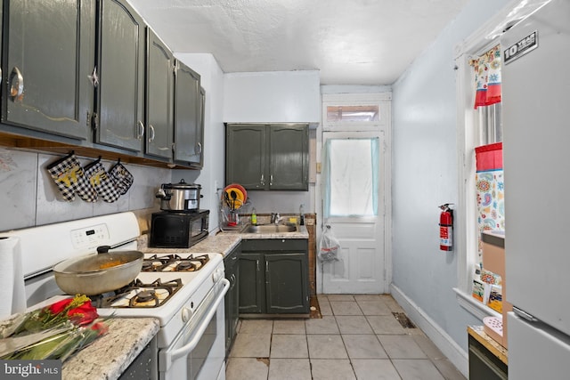 kitchen featuring white range with gas cooktop, light tile patterned floors, fridge, and gray cabinetry