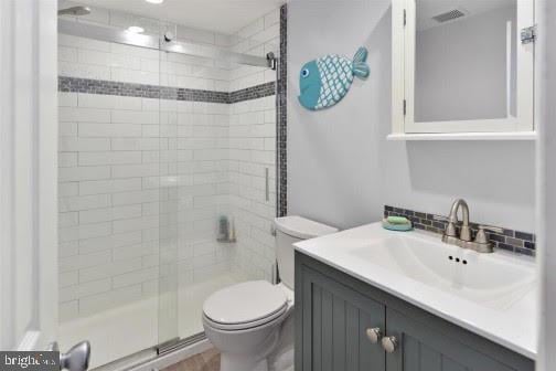 bathroom featuring a shower with door, vanity, and toilet